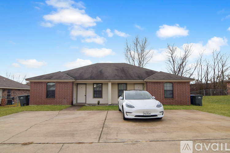 A white Tesla car is parked in front of a brick house.
