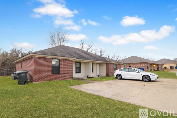 A white car is parked in front of a brick house.
