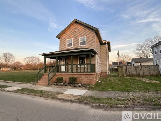 A house with a brown roof and a green porch is for sale.