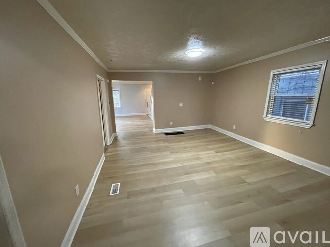 A spacious room with wooden flooring and a window on the right side.
