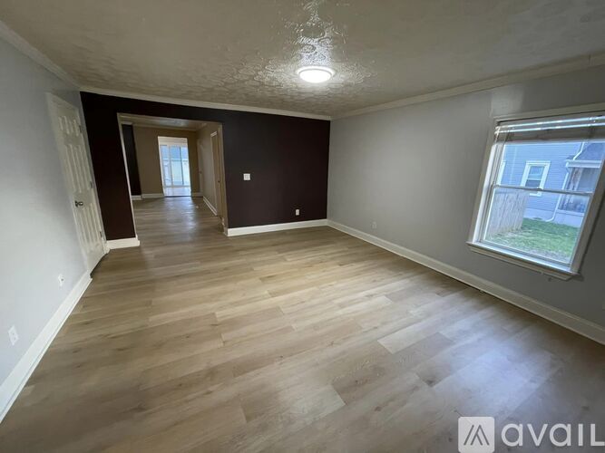 A spacious room with wooden flooring and a window on the right side.