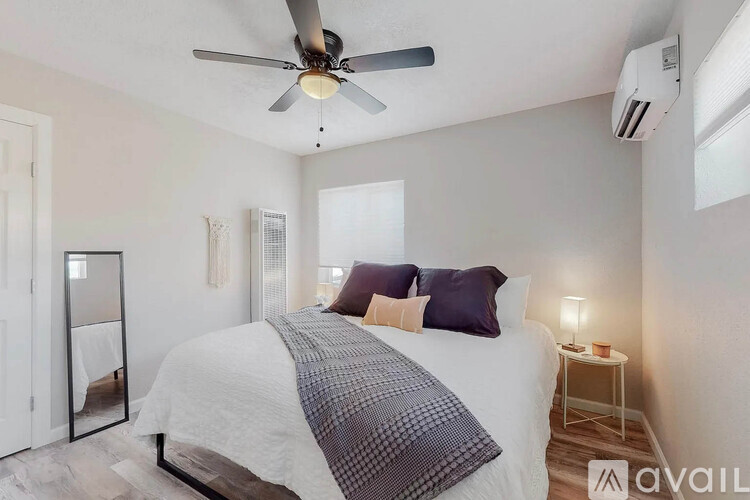 A bedroom with a bed, a ceiling fan, and a small table with a lamp.