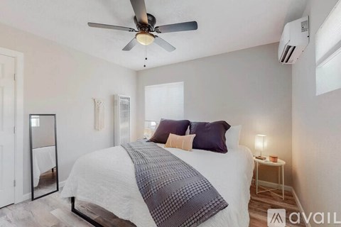 A bedroom with a bed, a ceiling fan, and a small table with a lamp.