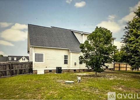 A house with a white exterior and a grey roof is surrounded by a wooden fence and a green lawn.