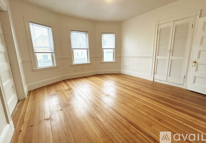 A room with wooden floors and three windows.