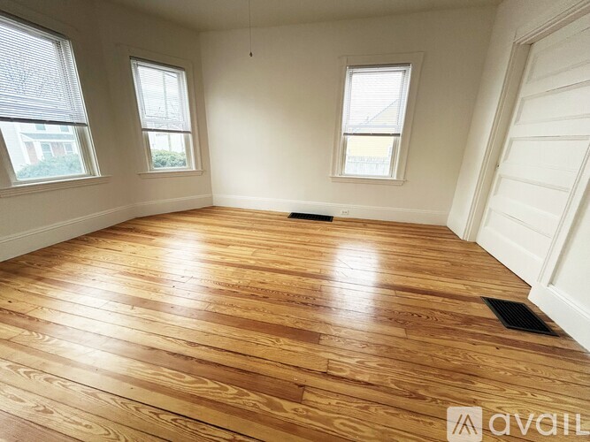 A room with wooden flooring and three windows.