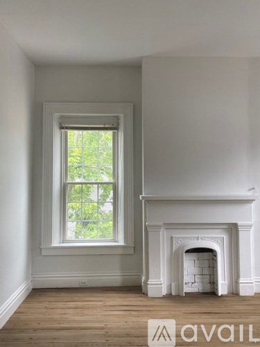 A white fireplace in a room with a window.