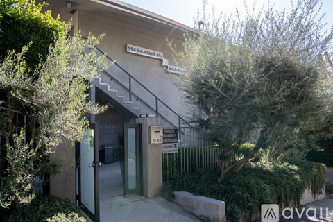 A building with a glass door and a sign that reads "1146 clark" is surrounded by greenery.