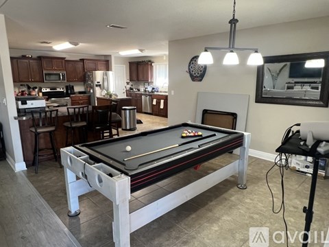 A pool table in a room with a kitchen in the background.