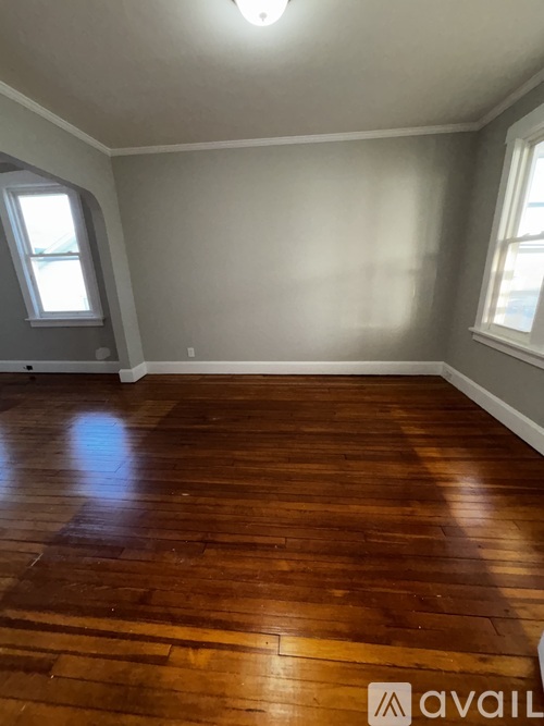 A room with wooden flooring and two windows.