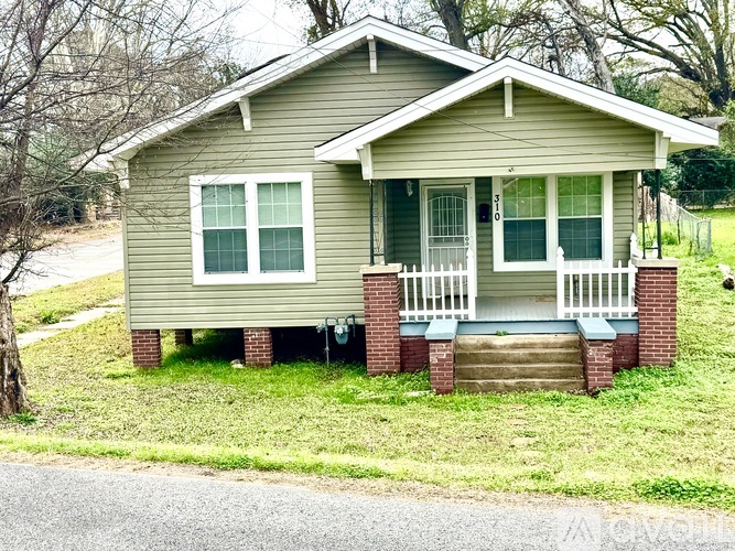 A small house with a porch and a green lawn.