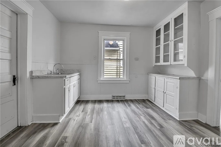 A kitchen with white cabinets and a window with blinds.