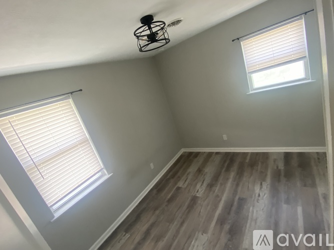 A room with a fan, two windows, and wooden flooring.