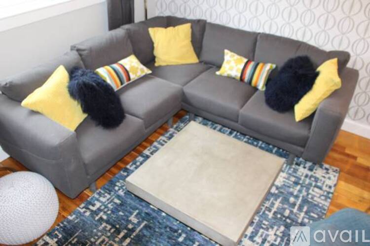 A grey couch with yellow pillows and a blue rug in front of it.