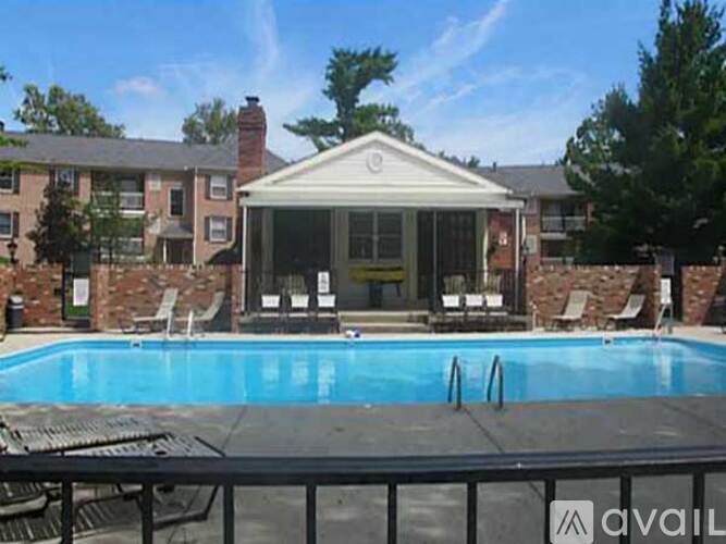 A pool in front of a house with a patio and chairs.