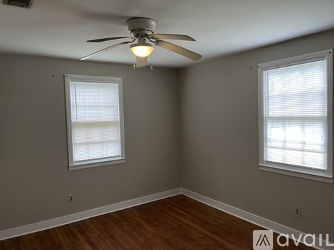 A room with a ceiling fan and two windows.