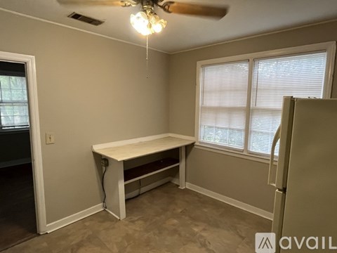 A room with a table, a ceiling fan, and a window with blinds.