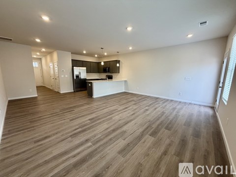 A spacious room with wooden flooring and a kitchen area in the background.