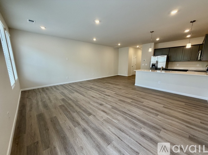 A spacious room with wooden flooring and a kitchen area in the background.