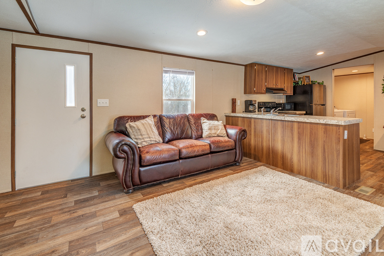 A brown leather couch sits in a living room with wooden floors and a white rug.