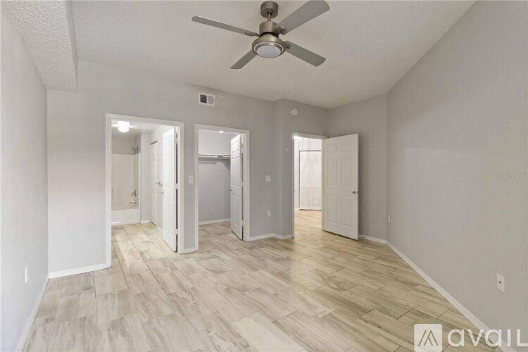 A spacious room with a ceiling fan and light, hardwood floors, and white walls with three open doors.