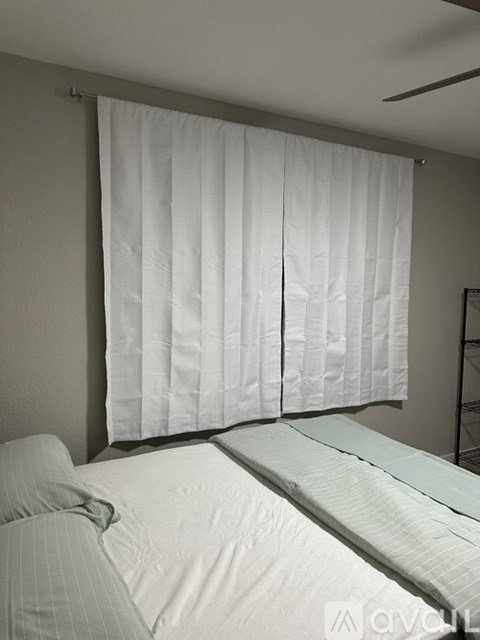 A bedroom with a bed and a window with white curtains.