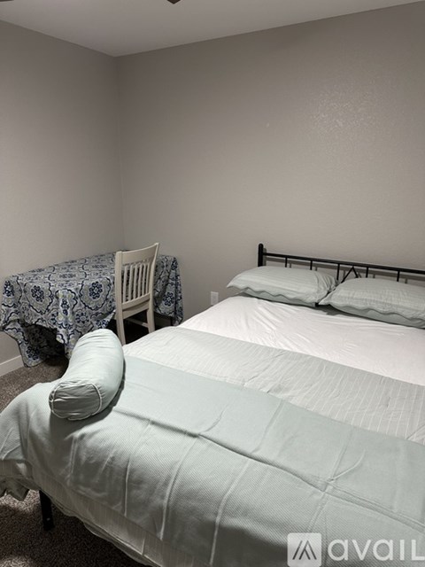 A bedroom with a bed, chair, and bedside table.