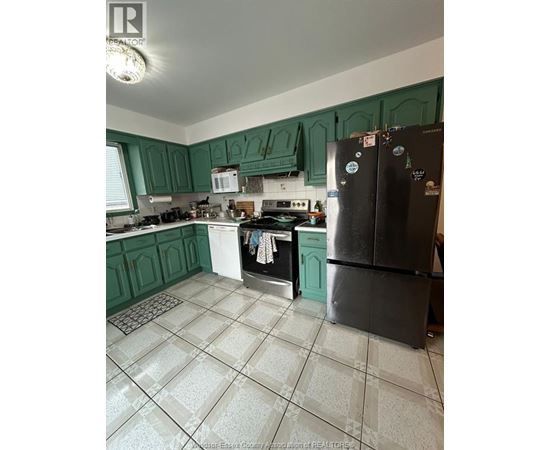 A kitchen with green cabinets and a black fridge.