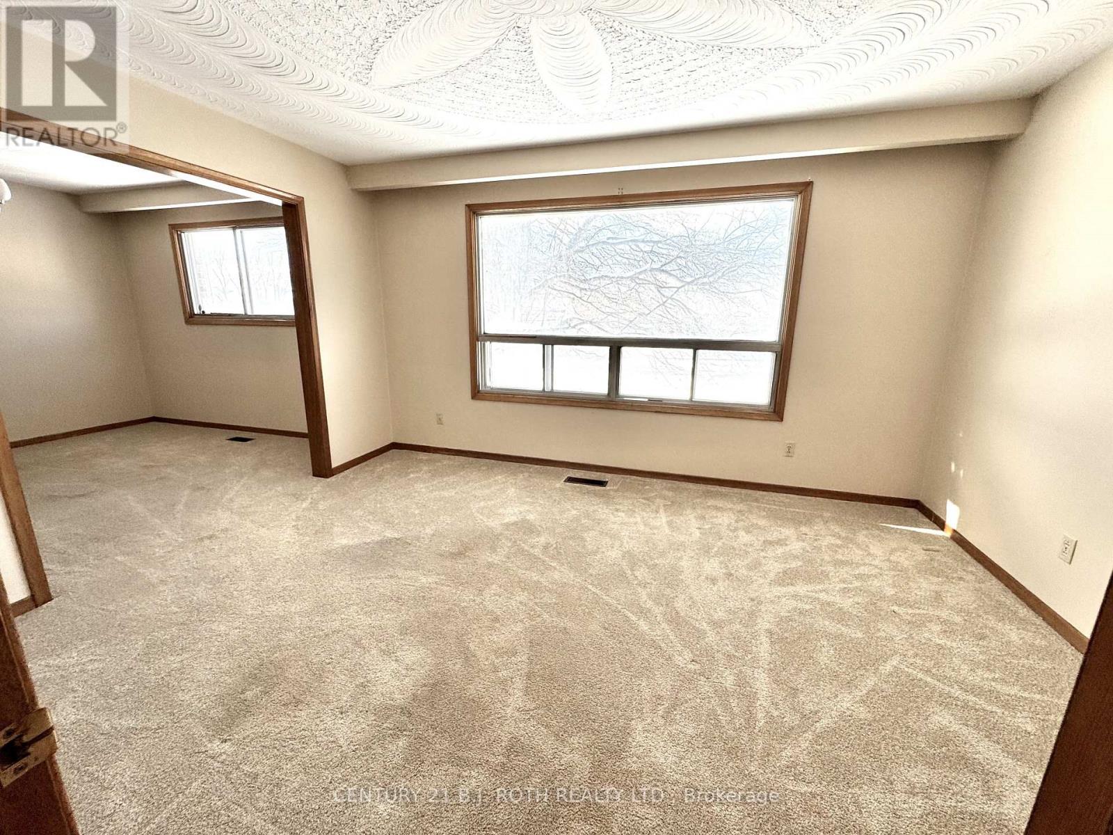 A room with a carpeted floor and two windows.