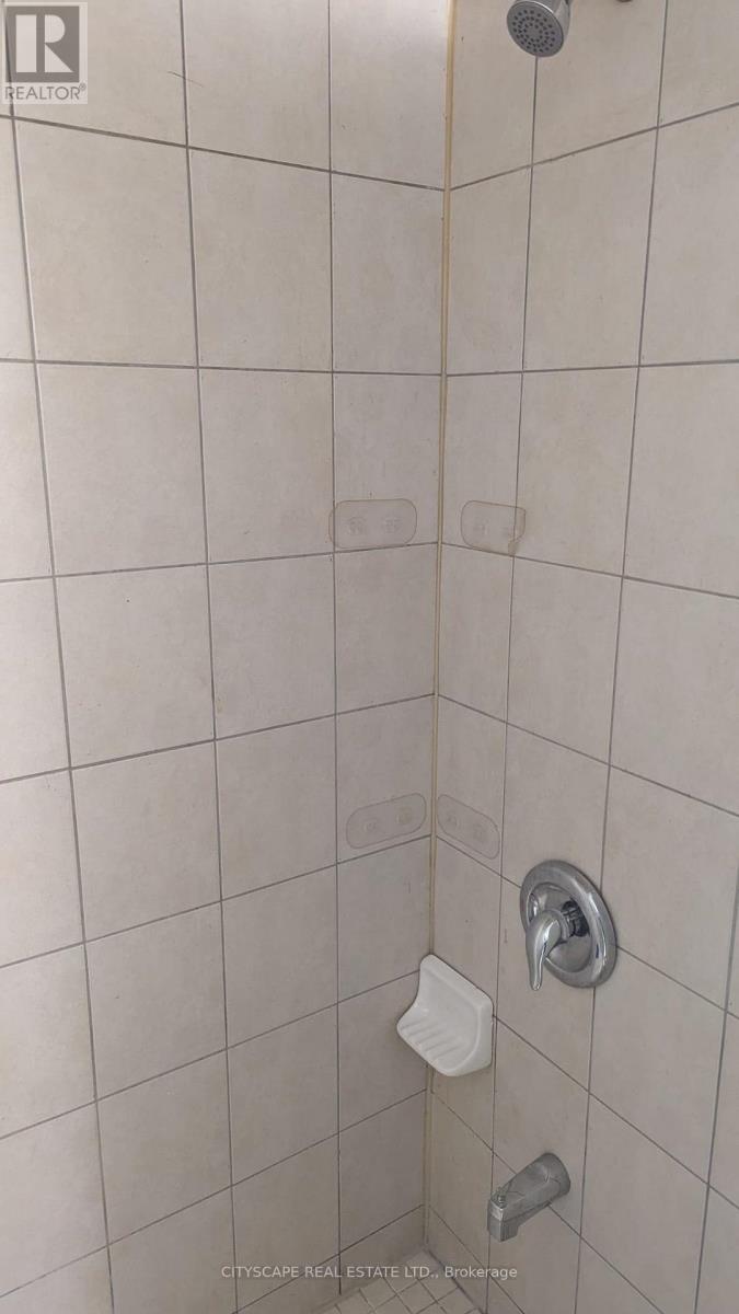 A shower with a white tile wall and a silver shower head.