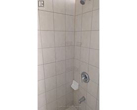 A shower with a white tile wall and a silver shower head.