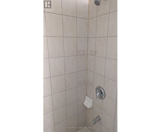 A shower with a white tile wall and a silver shower head.