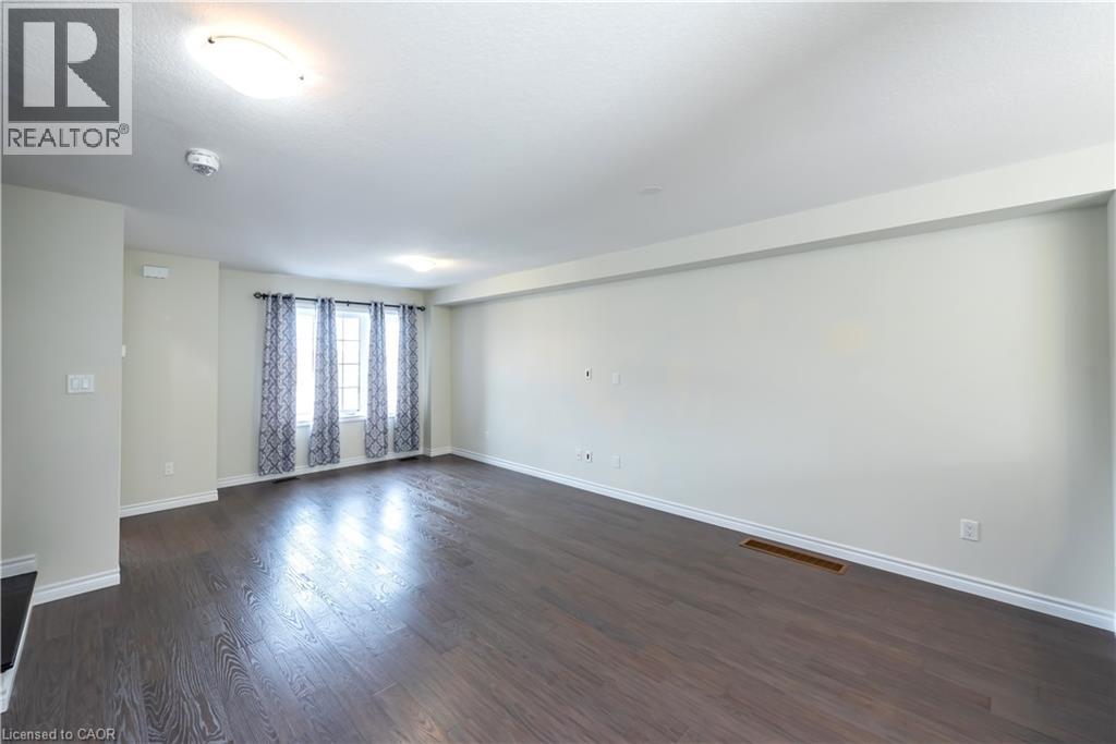 A spacious room with wooden flooring and a window with curtains.