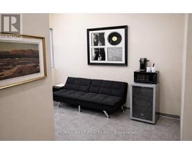 A black sofa sits in a room with a framed picture and a record player.