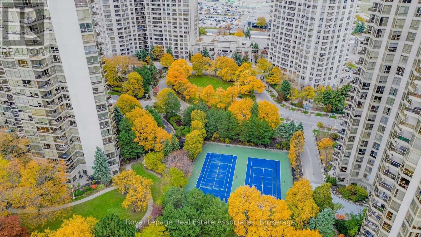 A tennis court surrounded by trees with autumn leaves.