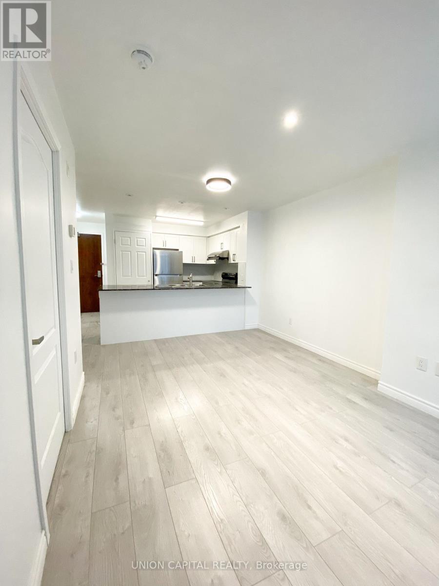 A spacious room with wooden flooring and a kitchen area in the background.