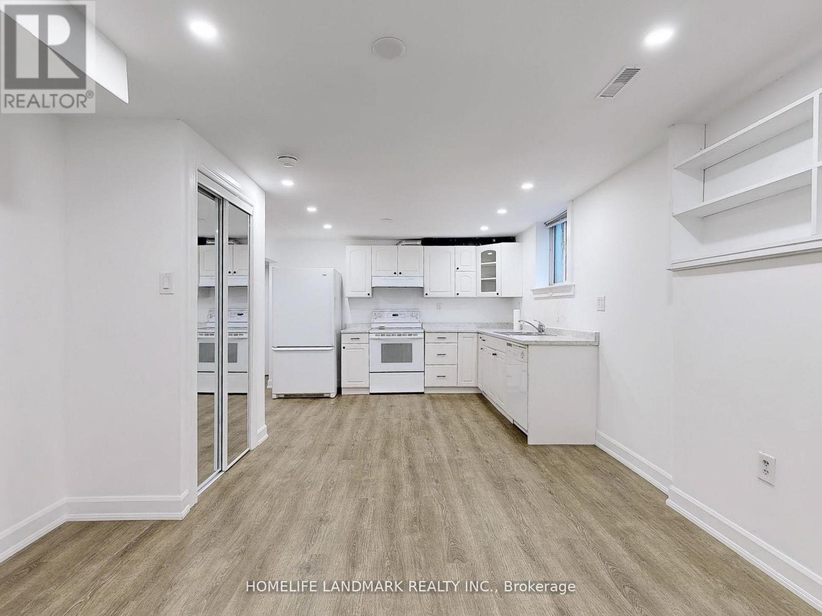 A well-lit, spacious kitchen with white appliances and wooden flooring.