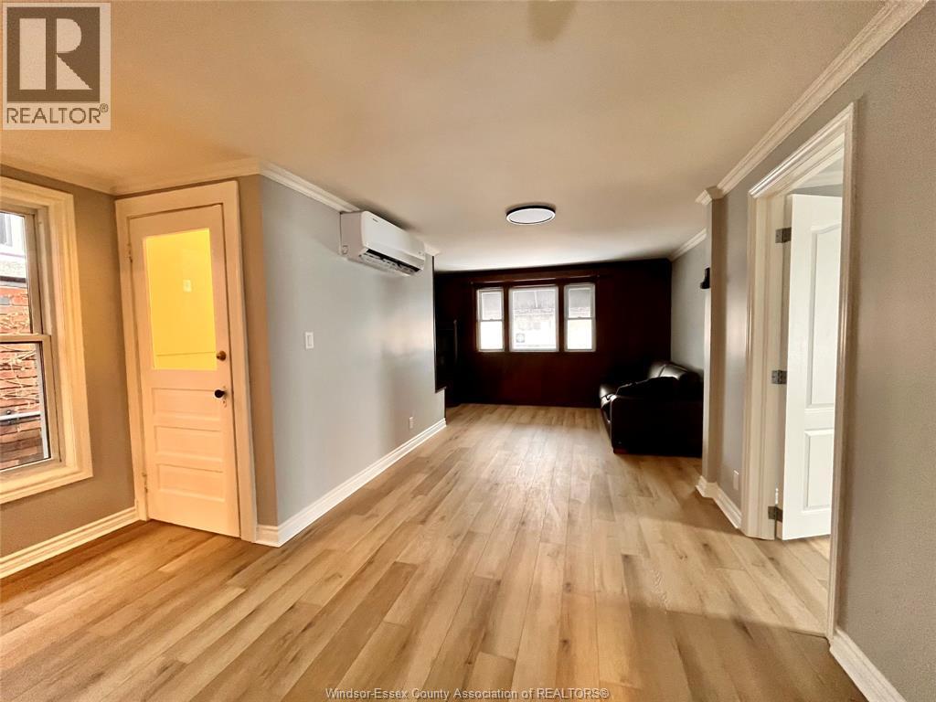 A spacious room with wooden flooring and a window with blinds.
