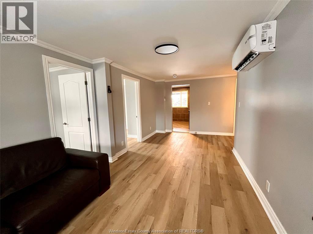 A brown leather couch sits in a room with wooden floors and white walls.