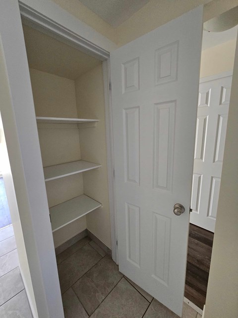 A white door is open to a small pantry with shelves.