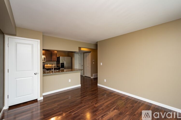 A room with wooden floors and a white door leading to a kitchen.