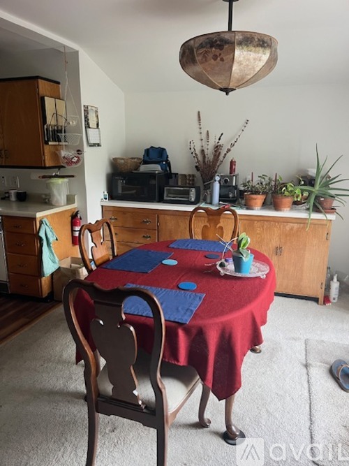 A dining room with a table covered in a red cloth and chairs around it.
