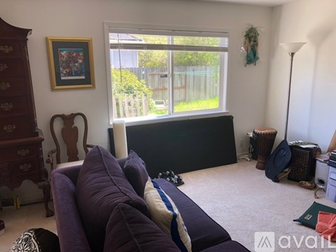 A living room with a purple couch and a window overlooking a fence.