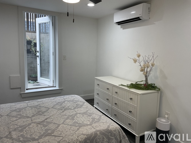 A white bedroom with a bed, dresser, and window.