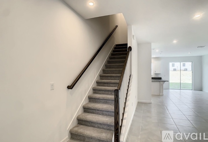 A staircase with a carpeted runner and wooden handrails leads to a bright open space.