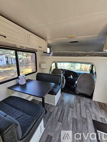 The image shows the interior of a camper van with a table, two chairs, and a bench.