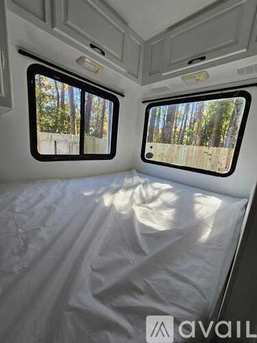 A white bedroom with two windows and a bed covered in a white sheet.