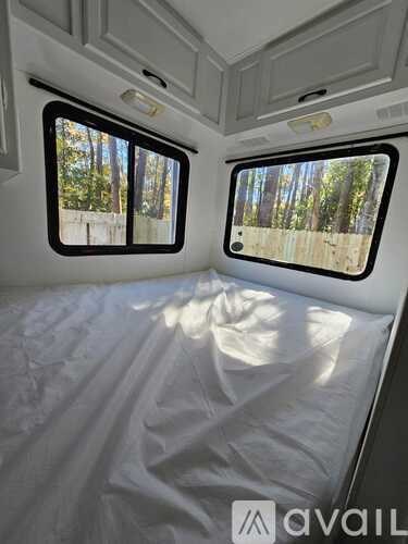 A white bedroom with two windows and a bed covered in a white sheet.