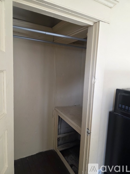 A white door is open to a small, empty room with a black refrigerator.