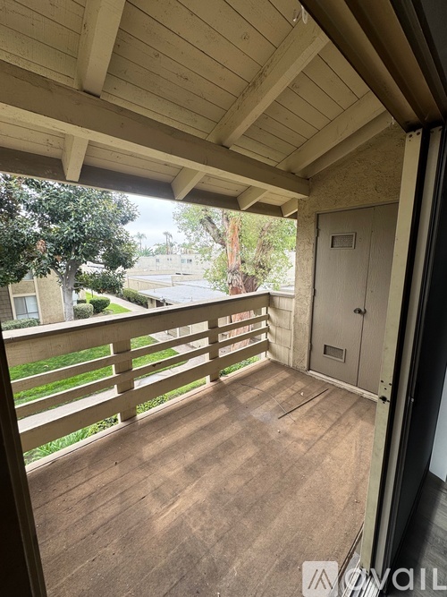 A balcony with a wooden floor and ceiling with a view of a tree and a building.